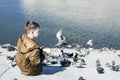 A child feeds pigeons bread on the shore of the lake