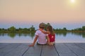 Boy with flat cap and little girl are sitting on pier. Little girl is a hug her older brother. Love, friendship and