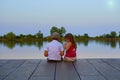 Boy with flat cap and little girl are sitting on pier. Love, friendship and childhood concept. Beautiful romantic sunset Royalty Free Stock Photo