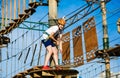 Boy in forest adventure park. Kid in orange helmet and white t shirt climbs on high rope trail. Climbing outdoor, amusement