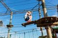 Boy in forest adventure park. Kid in orange helmet and white t shirt climbs on high rope trail. Climbing outdoor, amusement center