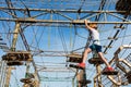 Boy in forest adventure park. Kid in orange helmet and white t shirt climbs on high rope trail. Climbing outdoor