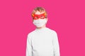 A boy with funny superhero mask to protect himself from viral infections of the disease, isolated on pink background