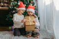 A boy and a girl in Christmas hats open a gift box under a Christmas tree. Celebration, receiving gifts, children`s joy. Miracle, Royalty Free Stock Photo