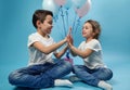Boy and girl clapping hands while posing on blue background with balloons behind them