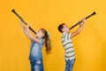 A boy and a girl with clarinets are standing with their backs to each other, playing the clarinet, on a yellow background