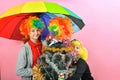 A boy and a girl in a clown wig hug a funny new year christmas tree in a wig under a colored umbrella Royalty Free Stock Photo