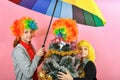 A boy and a girl in a clown wig stand next to a funny wig-wearing Christmas tree under a colored umbrella Royalty Free Stock Photo