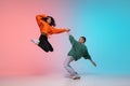 Boy and girl dancing hip-hop in stylish clothes on gradient background at dance hall in neon light. Royalty Free Stock Photo