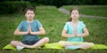 Boy and girl doing yoga, outdoors, on a background of green grass, sitting on a gymnastic mat Royalty Free Stock Photo