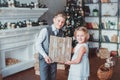 Boy and girl dressed elegantly standing in a bright room by the fireplace. Christmas tree in the background