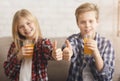 Boy And Girl Drinking Juice Gesturing Thumbs-Up Sitting On Sofa Royalty Free Stock Photo