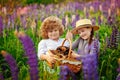 A boy and a girl in a hat holding a basket with a puppy, standing in a field with tall blue-purple flowers, a summer landscape. Royalty Free Stock Photo