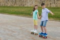 The boy and girl have joined hands and go on skateboards for a walk in the summer in the park