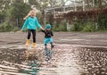 Boy and girl jumping in puddle in waterproof coat and rubber boots