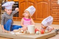 Boy and girl and a newborn kid with them in chef`s hats sitting on the kitchen floor soiled with flour