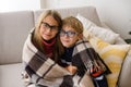 Boy and girl, an older sister and younger brother, are sitting under blanket on sofa, secreting, dreaming, hugging Royalty Free Stock Photo