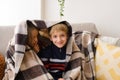 Boy and girl, an older sister and younger brother, are sitting under blanket on sofa, secreting, dreaming, hugging Royalty Free Stock Photo