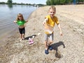 A boy and a girl are playing on the beach. Children play with water, sand and pebbles on the river bank. Kids are dressed in plain Royalty Free Stock Photo