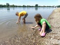 A boy and a girl are playing on the beach. Children play with water, sand and pebbles on the river bank. Kids are dressed in t- Royalty Free Stock Photo