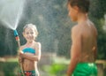 Boy and girl playing in garden, pouring with water each other from the hose, making a rain. Happy childhood concept image Royalty Free Stock Photo