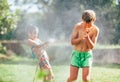 Boy and girl playing in garden, pouring with water each other from the hose, making a rain. Happy childhood concept image Royalty Free Stock Photo