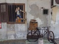 A boy and a girl reach out of the window to a basket on a Bicycle. 3D mural art in Georgetown.