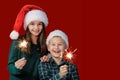 Boy and girl in Santa Claus hats on a red background holding sparklers in their hands Royalty Free Stock Photo