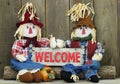 Boy and girl scarecrows sitting on log holding red wood welcome sign