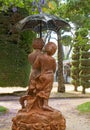 A boy and girl shelter under an umbrella fountain amongst the tree foliage.