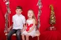 boy and girl - sister and brother - sitting on a swing decorated with christmas decor and tree branches. on red Royalty Free Stock Photo