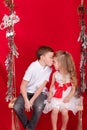 boy and girl - sister and brother - sitting on a swing decorated with christmas decor and tree branches. on red Royalty Free Stock Photo