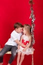 boy and girl - sister and brother - sitting on a swing decorated with christmas decor and tree branches. on red Royalty Free Stock Photo