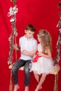 boy and girl - sister and brother - sitting on a swing decorated with christmas decor and tree branches. on red Royalty Free Stock Photo