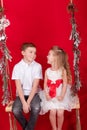 boy and girl - sister and brother - sitting on a swing decorated with christmas decor and tree branches. on red Royalty Free Stock Photo