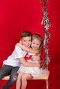 boy and girl - sister and brother - sitting on a swing decorated with christmas decor and tree branches. on red Royalty Free Stock Photo