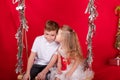 boy and girl - sister and brother - sitting on a swing decorated with christmas decor and tree branches. on red Royalty Free Stock Photo