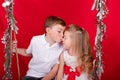 boy and girl - sister and brother - sitting on a swing decorated with christmas decor and tree branches. on red Royalty Free Stock Photo