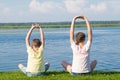 A boy and a girl are sitting on the green grass and doing yoga, holding their hands above their heads, rear view, against the Royalty Free Stock Photo