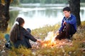 Boy and girl sitting on the river Bank, make a fire, autumn forest at sunset, beautiful nature and reflection of trees in the wate Royalty Free Stock Photo