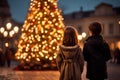 A boy and a girl are standing in front of a big Christmas tree in the city square Royalty Free Stock Photo
