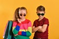 Boy and girl in sun glasses and with shopping bags, on a yellow background Royalty Free Stock Photo