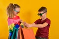 Boy and girl in sun glasses and with shopping bags, on a yellow background Royalty Free Stock Photo
