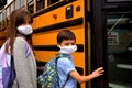 Coronavirus reopening school: A boy and girl wearing facemasks getting on a school bus