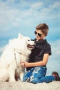 Happy 11 year old boy playing with his dog breed Samoyed at the seashore against a blue sky close up. Best friends rest Royalty Free Stock Photo