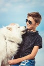 Happy 11 year old boy playing with his dog breed Samoyed at the seashore against a blue sky close up. Best friends rest Royalty Free Stock Photo