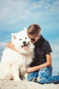 Happy 11 year old boy playing with his dog breed Samoyed at the seashore against a blue sky close up. Best friends rest Royalty Free Stock Photo