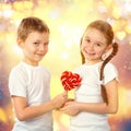 Boy gives a little girl candy red lollipop in heart shape. Valentine`s day art portrait. Royalty Free Stock Photo