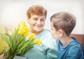 Boy giving a bunch of yellow flowers tulipan to grandmother. Grandson and grandma spending time together. Kindness to senior.