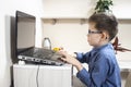 Boy in glasses and a blue shirt is sitting at a desk in front of a laptop and playing a computer game. Royalty Free Stock Photo